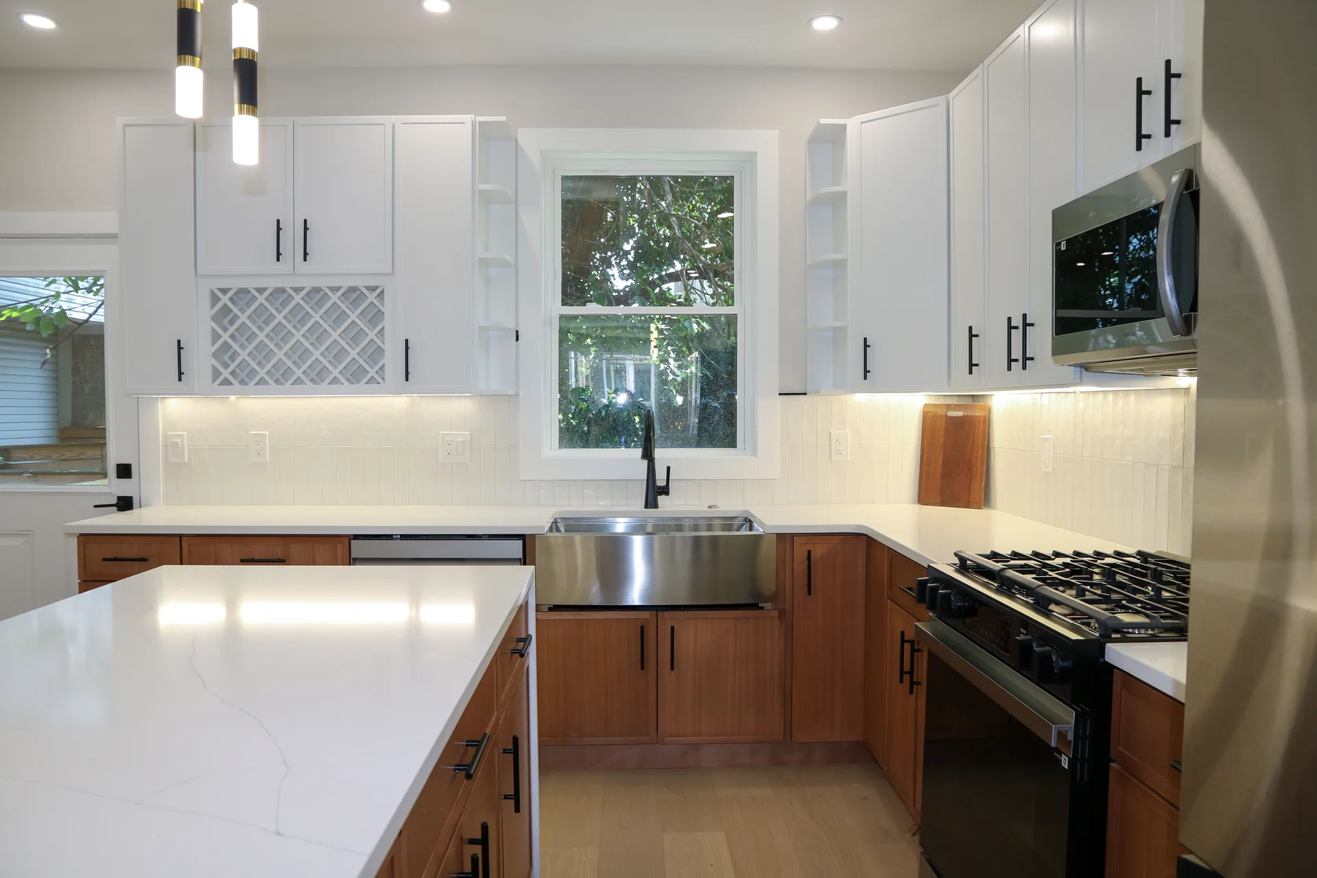 Two-tone kitchen with stainless farmhouse sink and quartz island