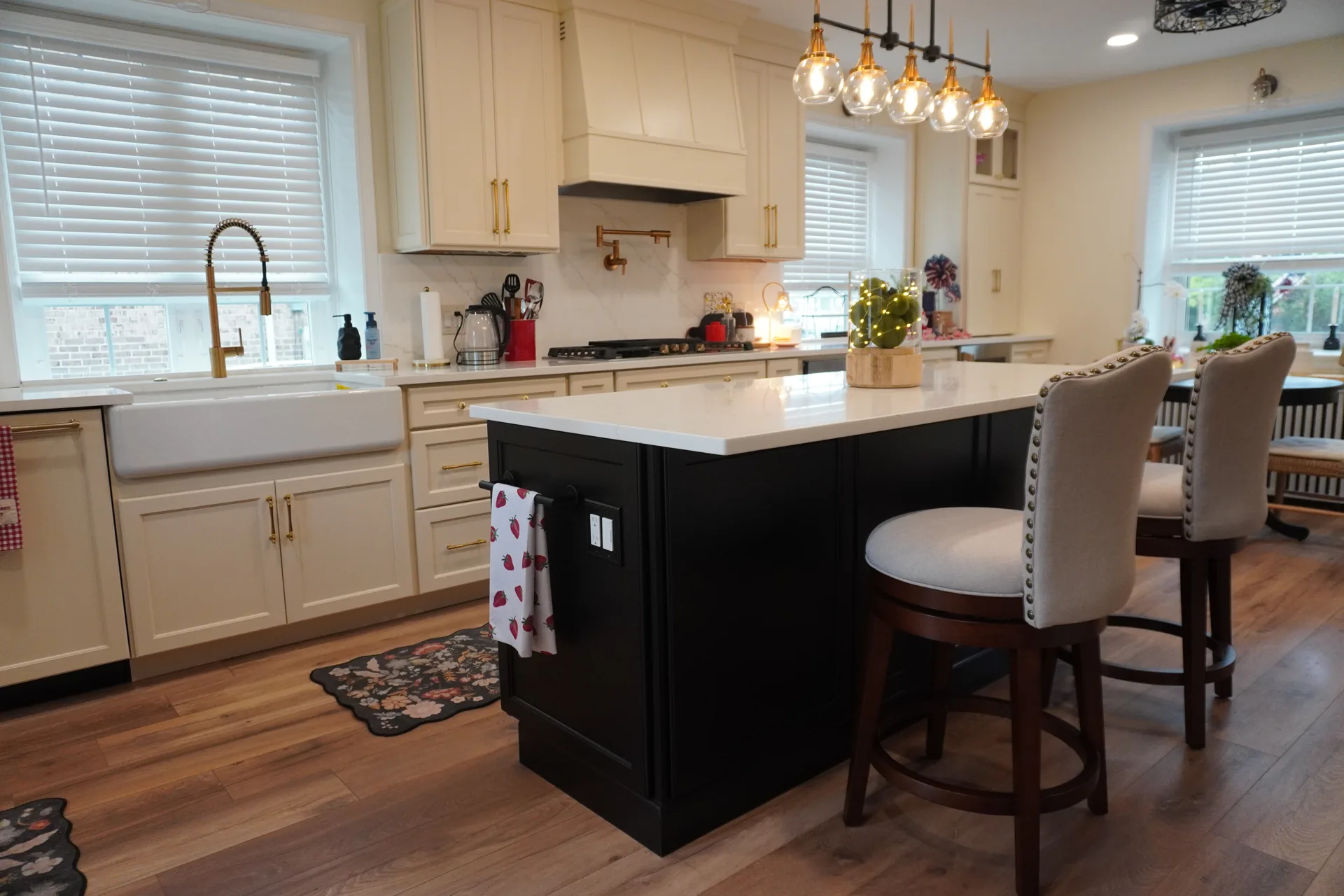 Cream kitchen with black island, upholstered bar stools, and brass fixtures