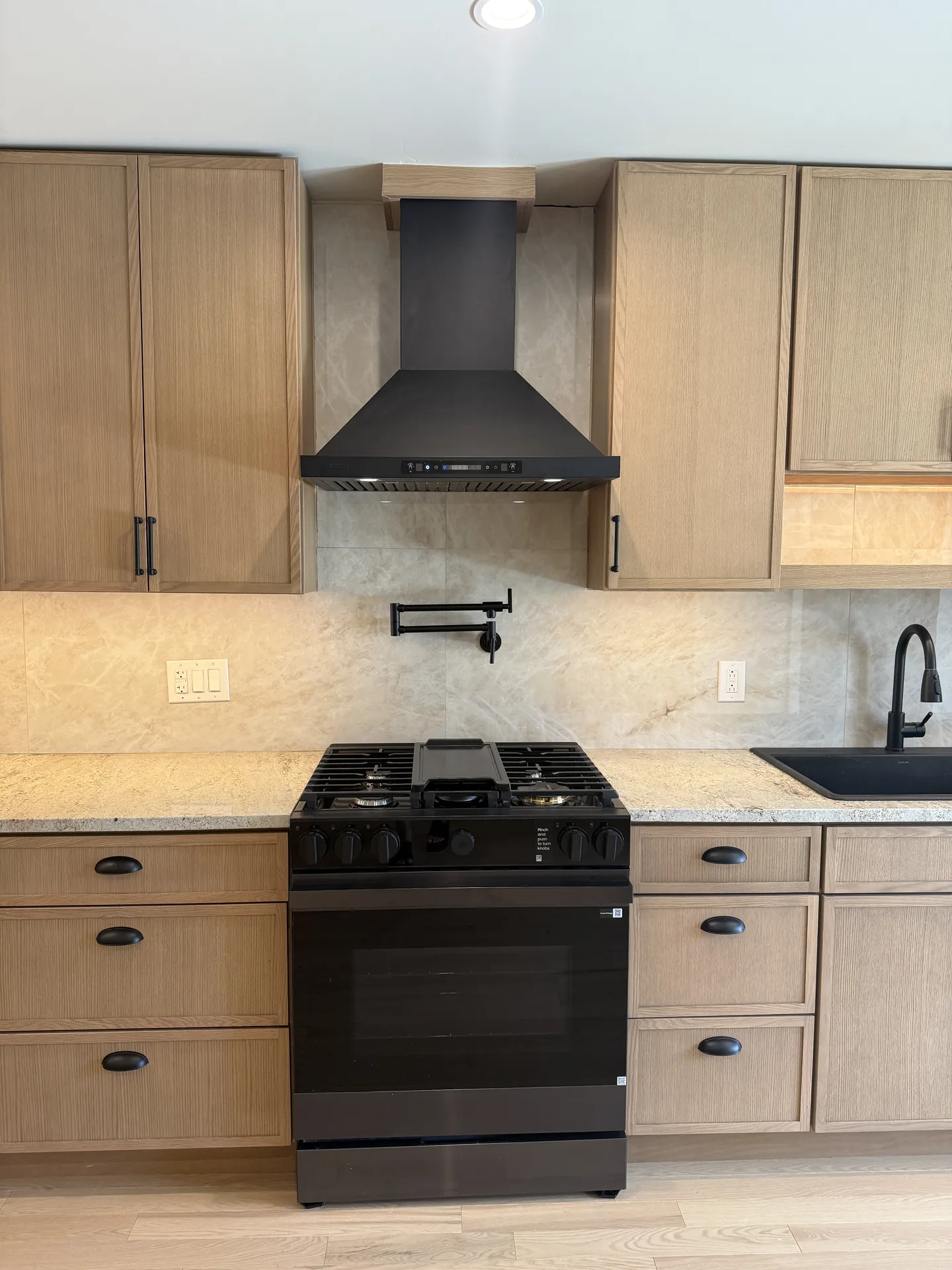 Light oak kitchen with black gas range, black hood, and quartzite counters