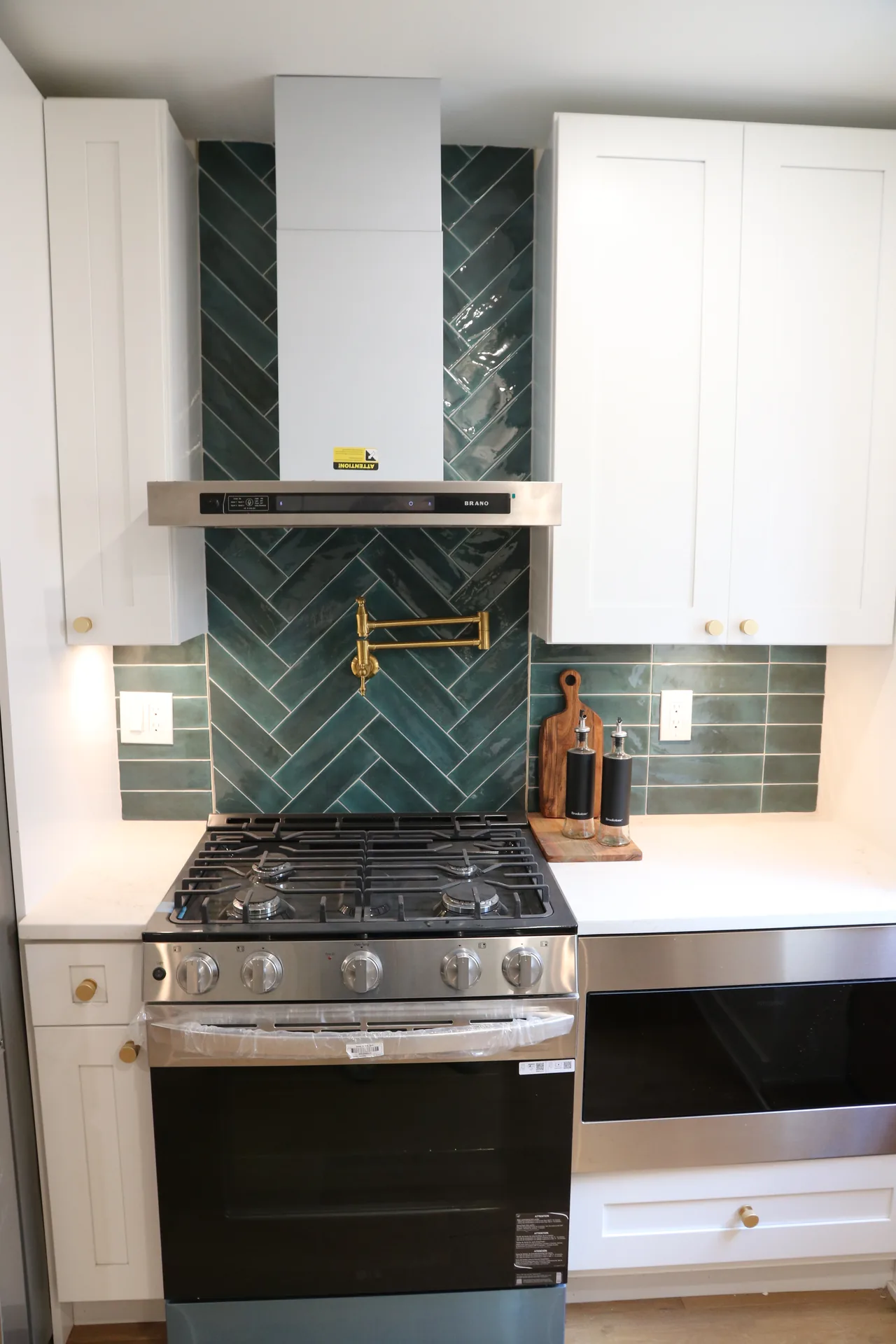 White shaker kitchen with green herringbone backsplash, pot filler, and gold hardware