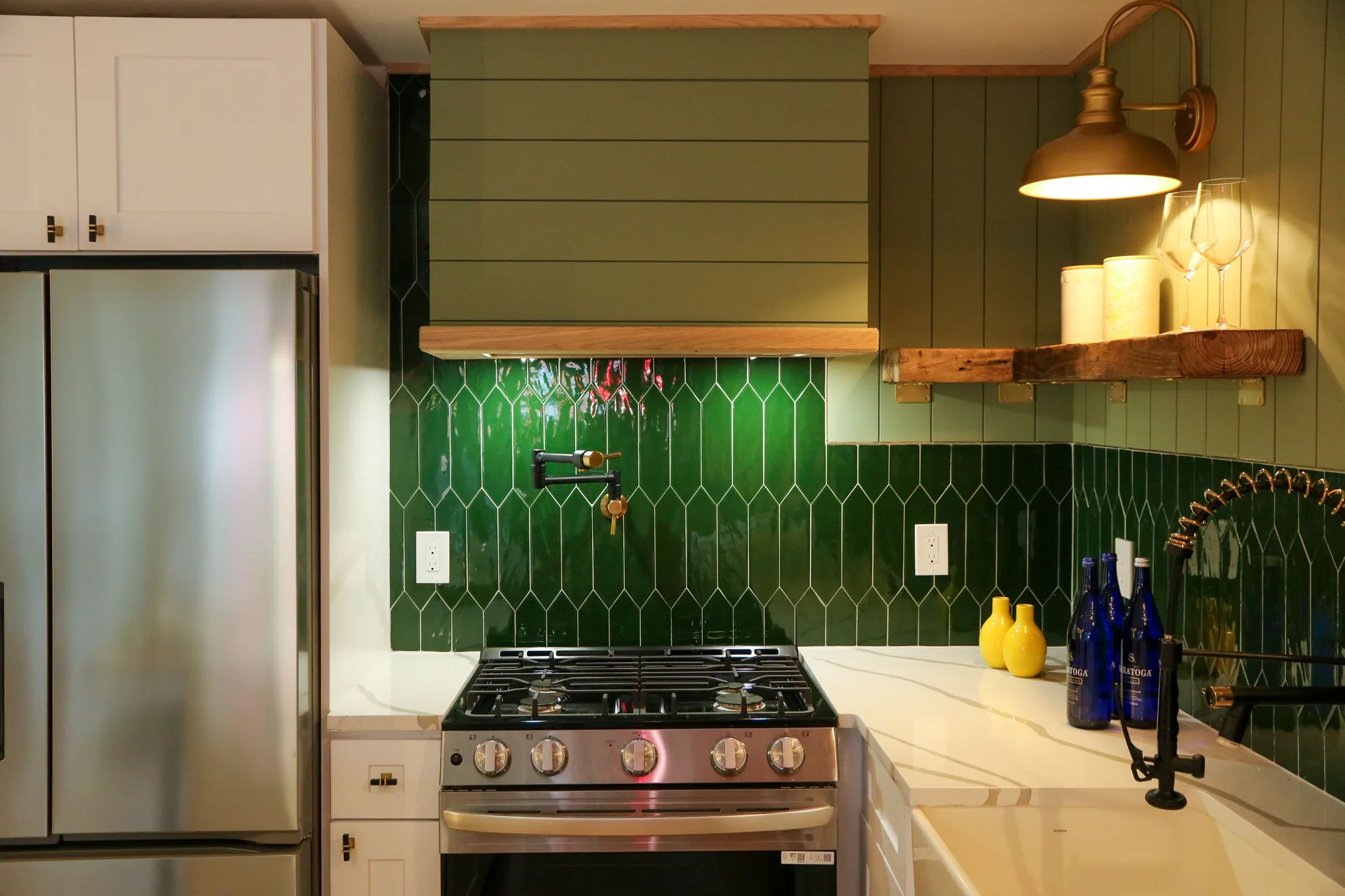 Gas range with green tile backsplash, wood hood, and brass lighting