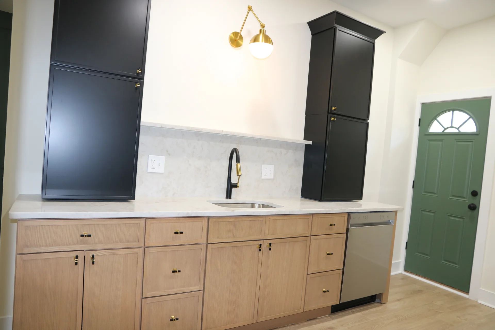 Light oak kitchen with black accent pantry, brass sconce, and marble backsplash