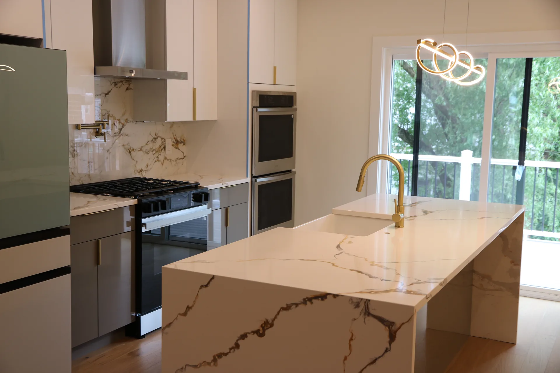 Waterfall quartz island with gold-veined marble backsplash and brass faucet