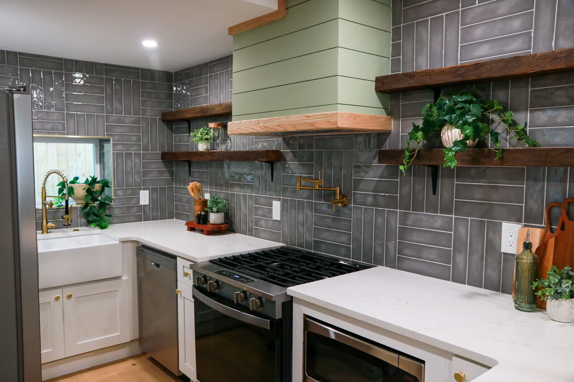 Kitchen with slate grey stacked tile, sage green range hood, and reclaimed wood floating shelves