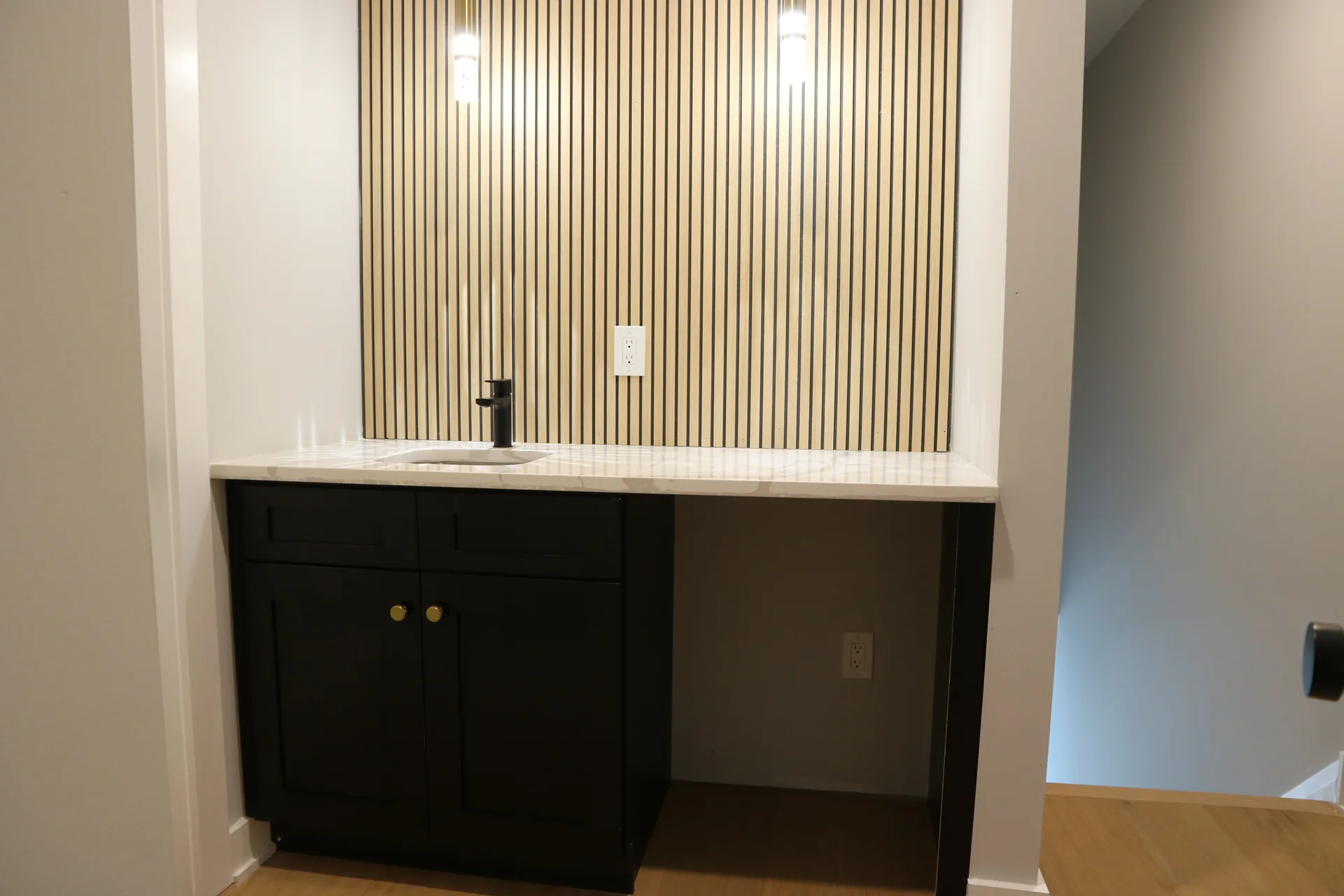 Wet bar with black cabinets, marble counter, and fluted wood slat wall